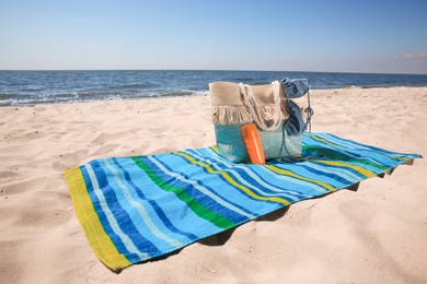 Photo of Striped beach towel and bag with accessories on sandy seashore