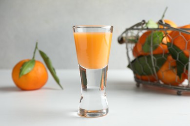Photo of Tasty tangerine liqueur in shot glass and fresh fruits on white table