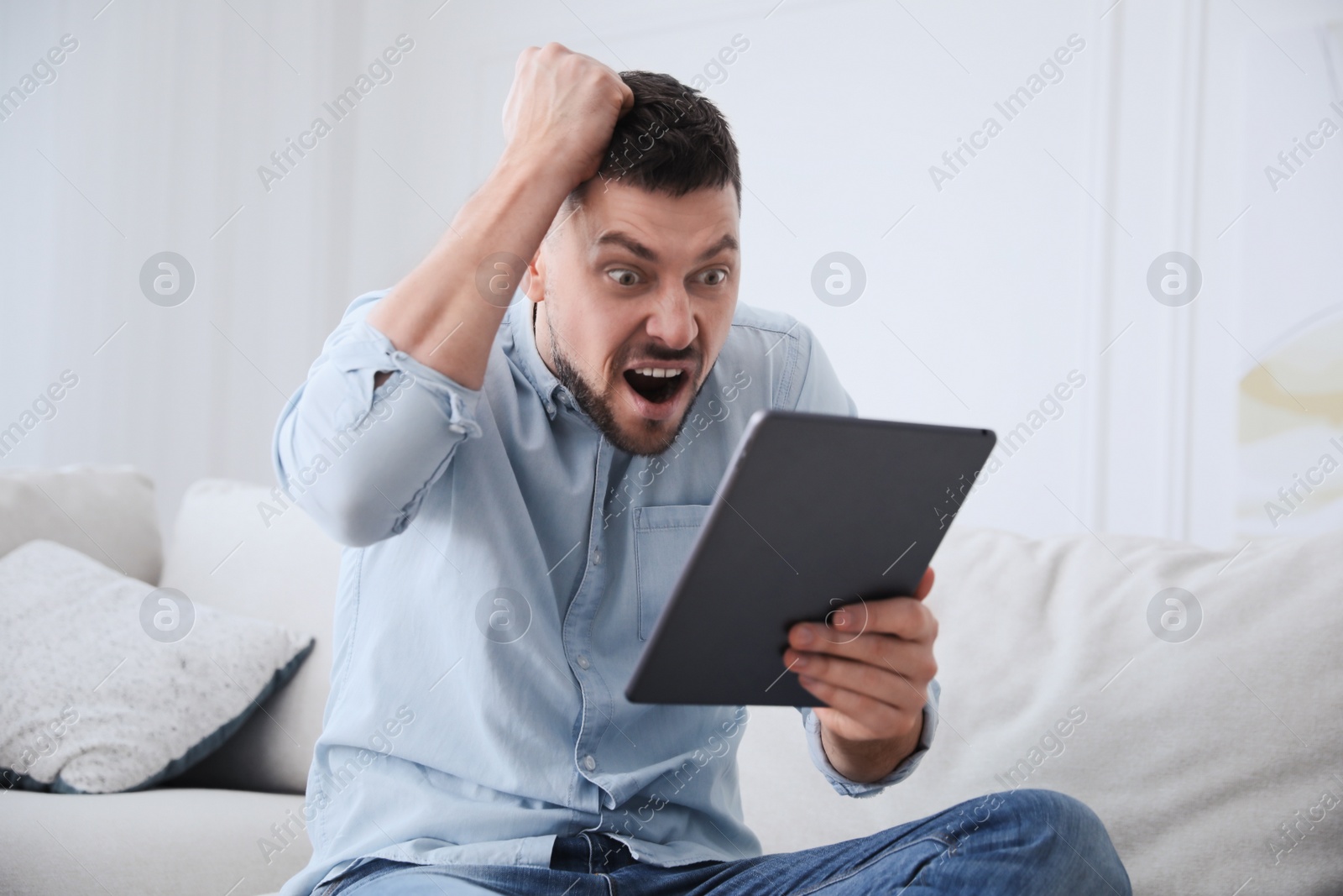 Photo of Emotional man with tablet at home. Online hate concept