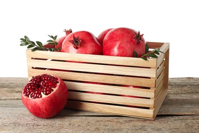 Fresh pomegranates and green leaves in box on wooden table against white background