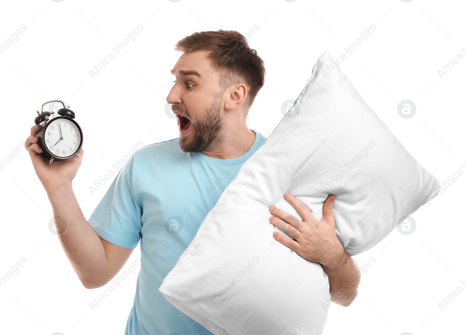 Photo of Emotional overslept man with alarm clock and pillow on white background. Being late concept