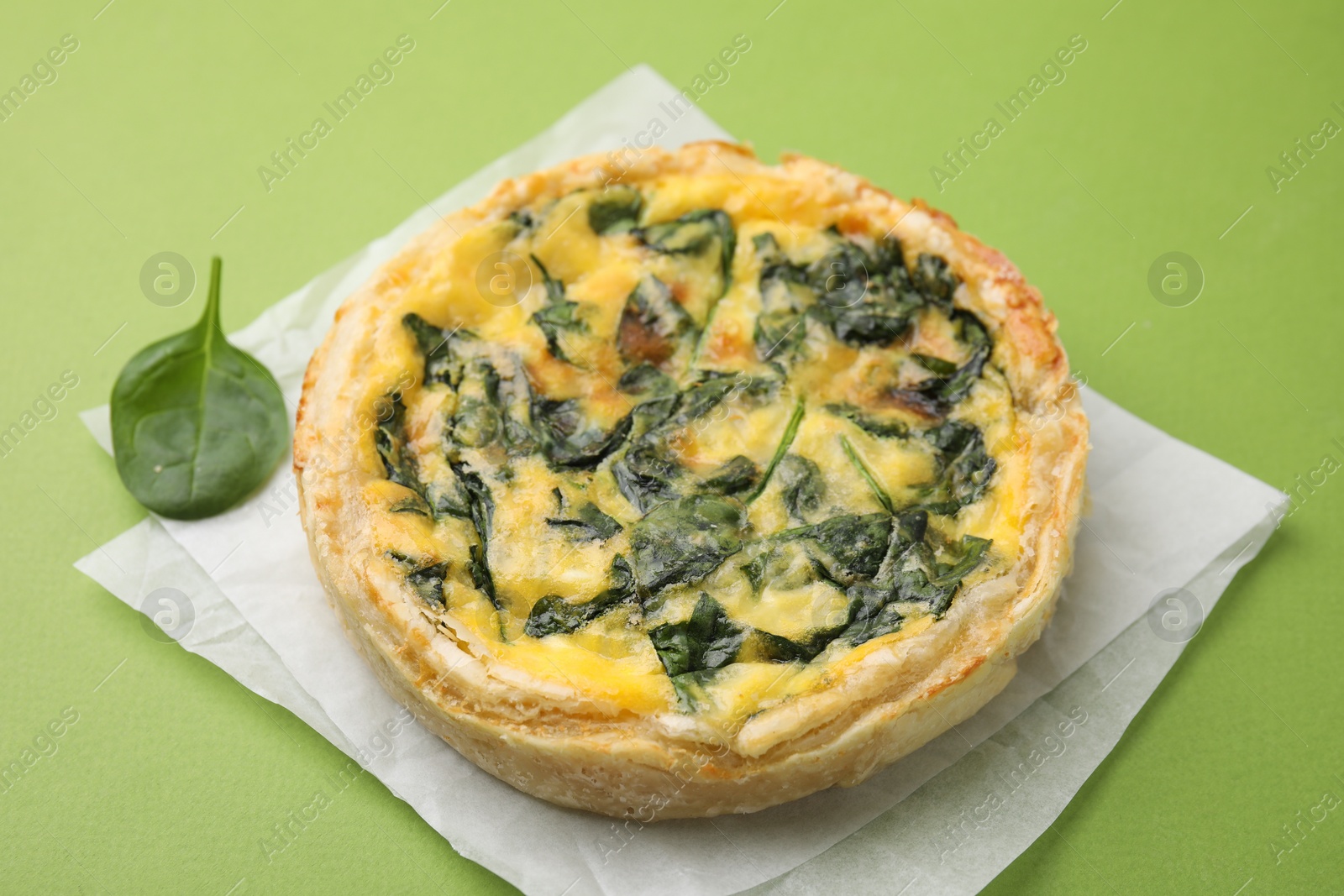 Photo of Delicious pie with spinach on green background, closeup