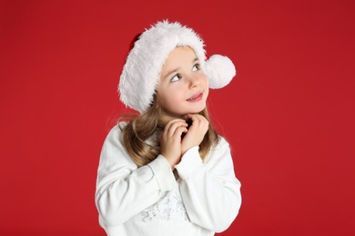 Cute child in Santa hat on red background. Christmas celebration