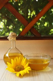Photo of Organic sunflower oil and flower on white wooden table