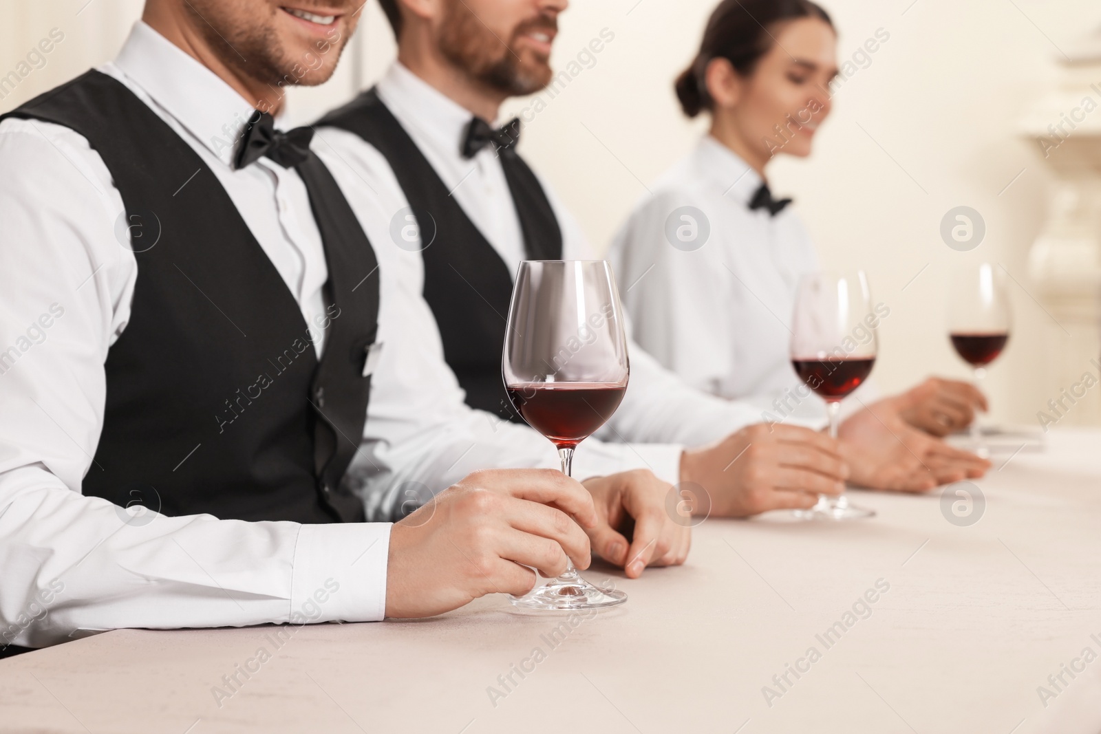 Photo of People with glasses of red wine at table indoors, closeup. Professional butler courses