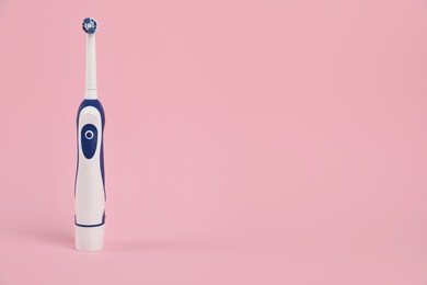 Electric toothbrush on pink background, space for text