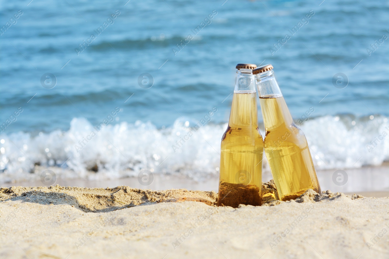 Photo of Bottles of cold beer on sandy beach near sea, space for text