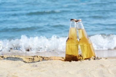 Photo of Bottles of cold beer on sandy beach near sea, space for text