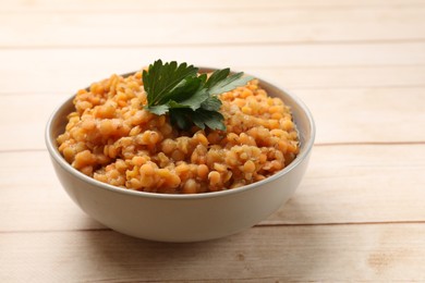 Photo of Delicious red lentils with parsley in bowl on wooden table, closeup. Space for text