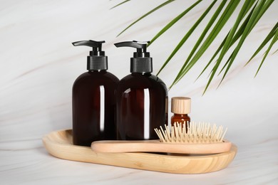 Shampoo bottles, wooden brush and essential oil on white marble table