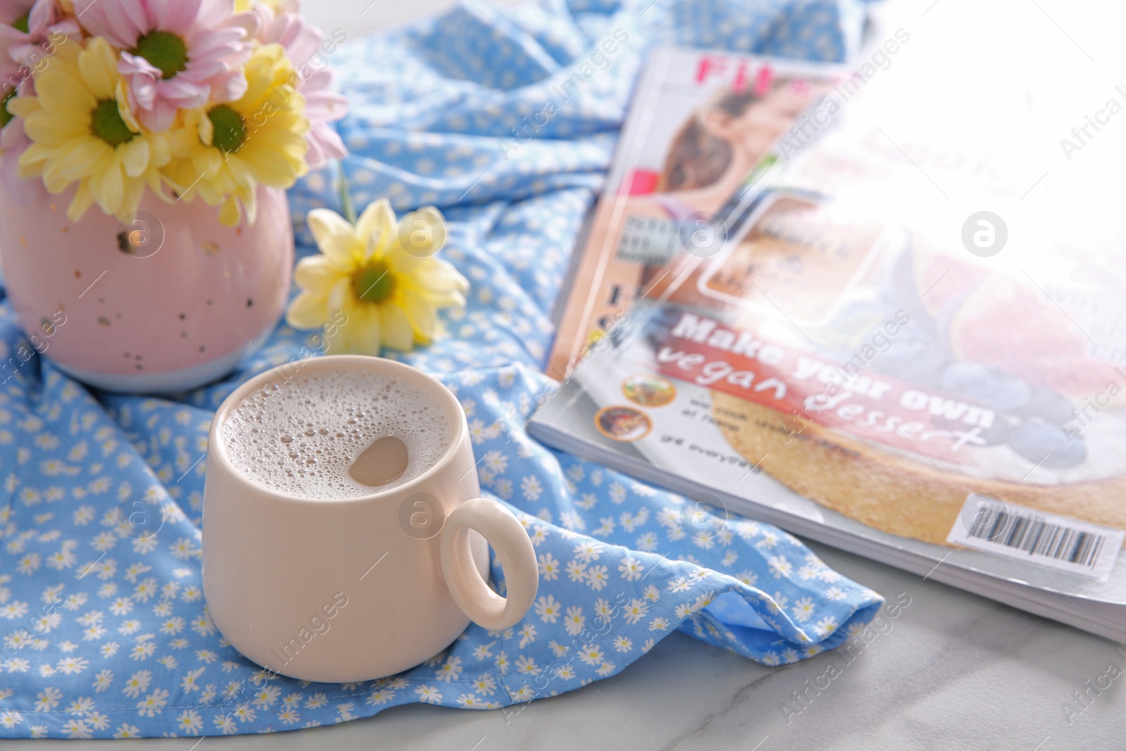 Photo of Cup of fresh coffee, beautiful bouquet and magazines on light blue printed cloth, space for text. Good morning