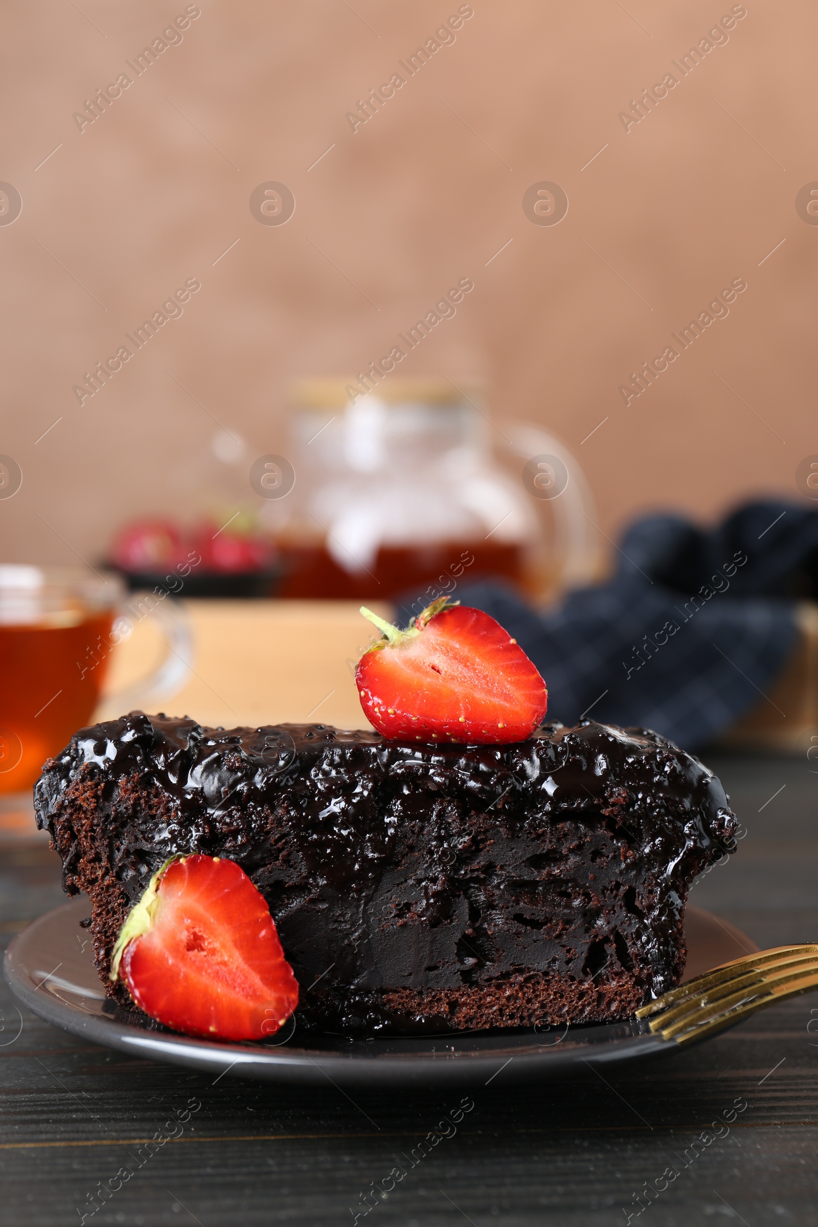 Photo of Piece of tasty chocolate sponge cake with strawberries on black wooden table, closeup