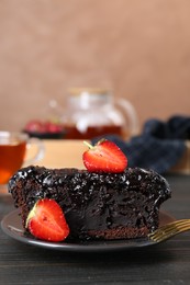 Piece of tasty chocolate sponge cake with strawberries on black wooden table, closeup