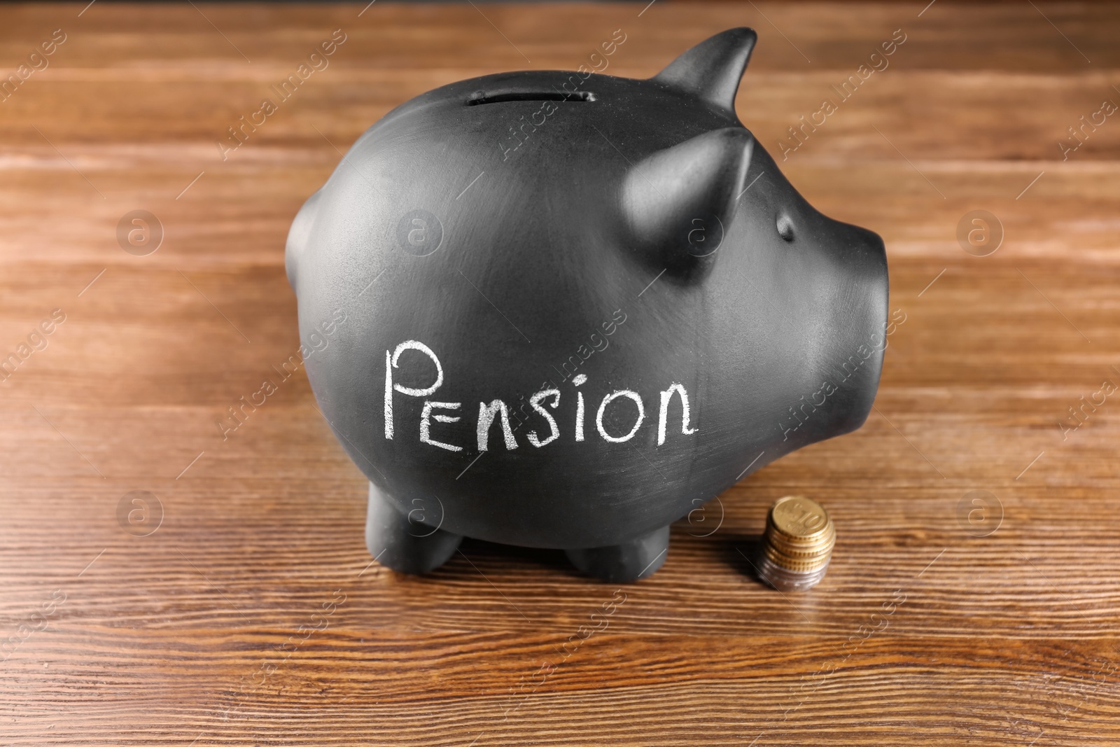 Photo of Black piggy bank with word "PENSION" and coins on wooden table