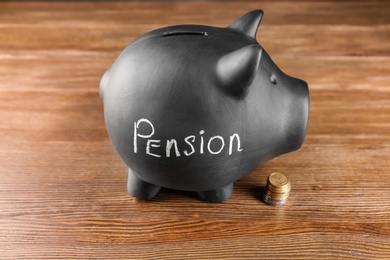 Black piggy bank with word "PENSION" and coins on wooden table