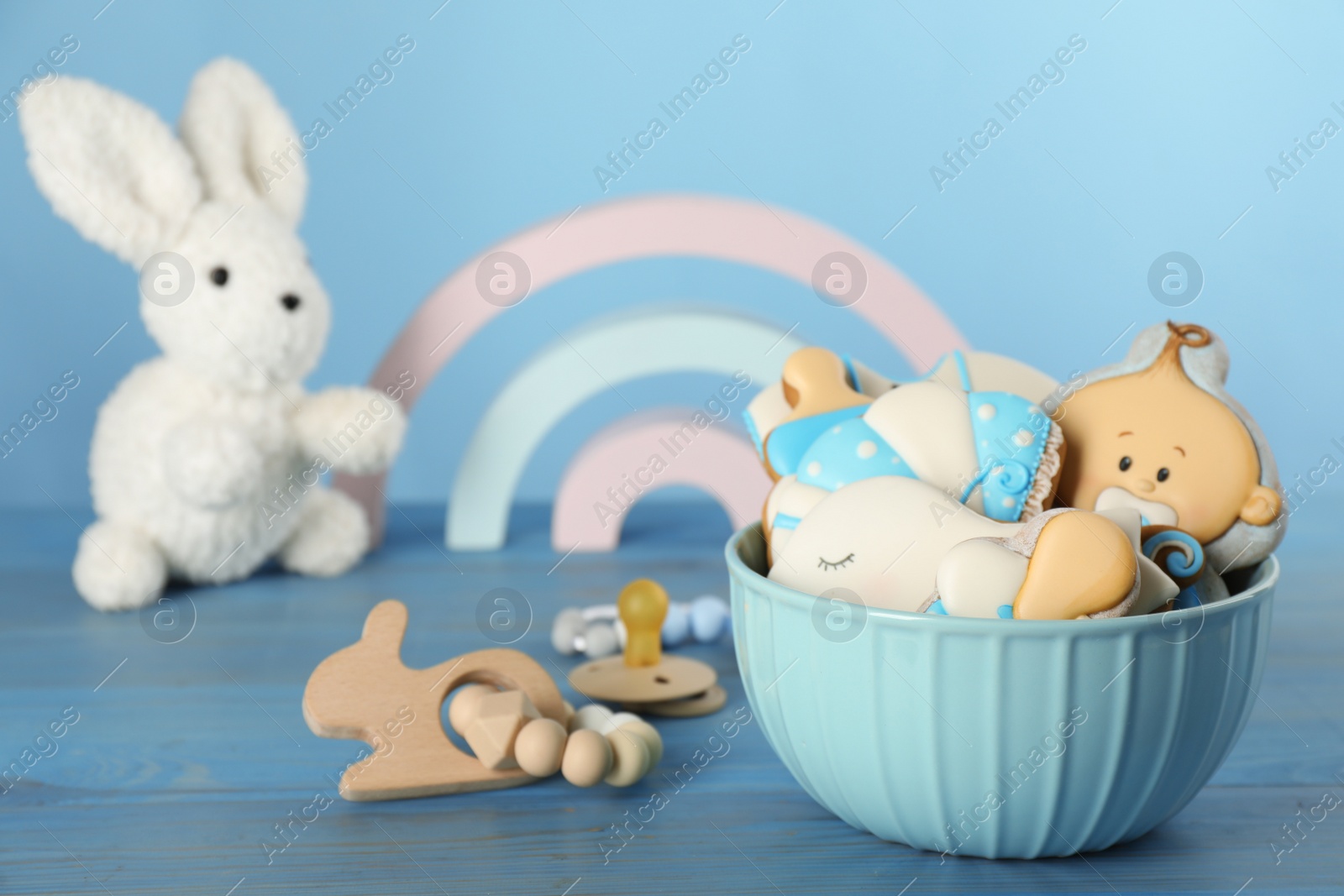 Photo of Cute tasty cookies of different shapes, pacifier and toys on light blue wooden table. Baby shower party