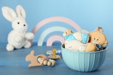 Cute tasty cookies of different shapes, pacifier and toys on light blue wooden table. Baby shower party