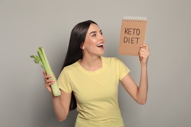 Photo of Emotional woman holding celery and notebook with words Keto Diet on light grey background
