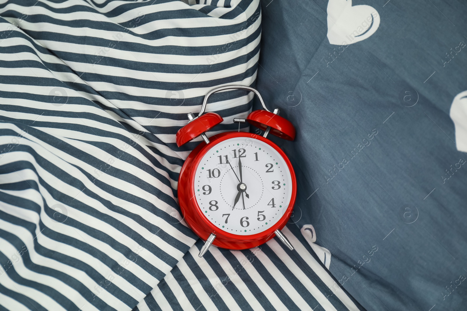 Photo of Analog alarm clock on bed, top view. Time of day