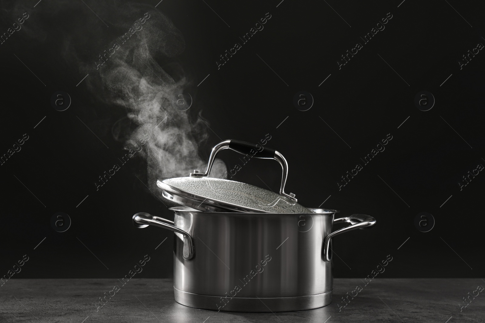 Photo of Steaming saucepot on grey table against dark background