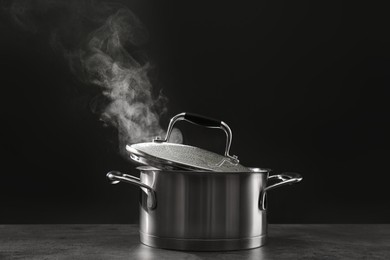Steaming saucepot on grey table against dark background