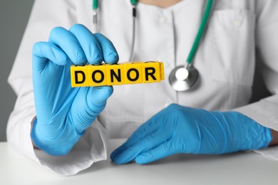 Photo of Doctor holding word Donor made of cubes at white table, closeup