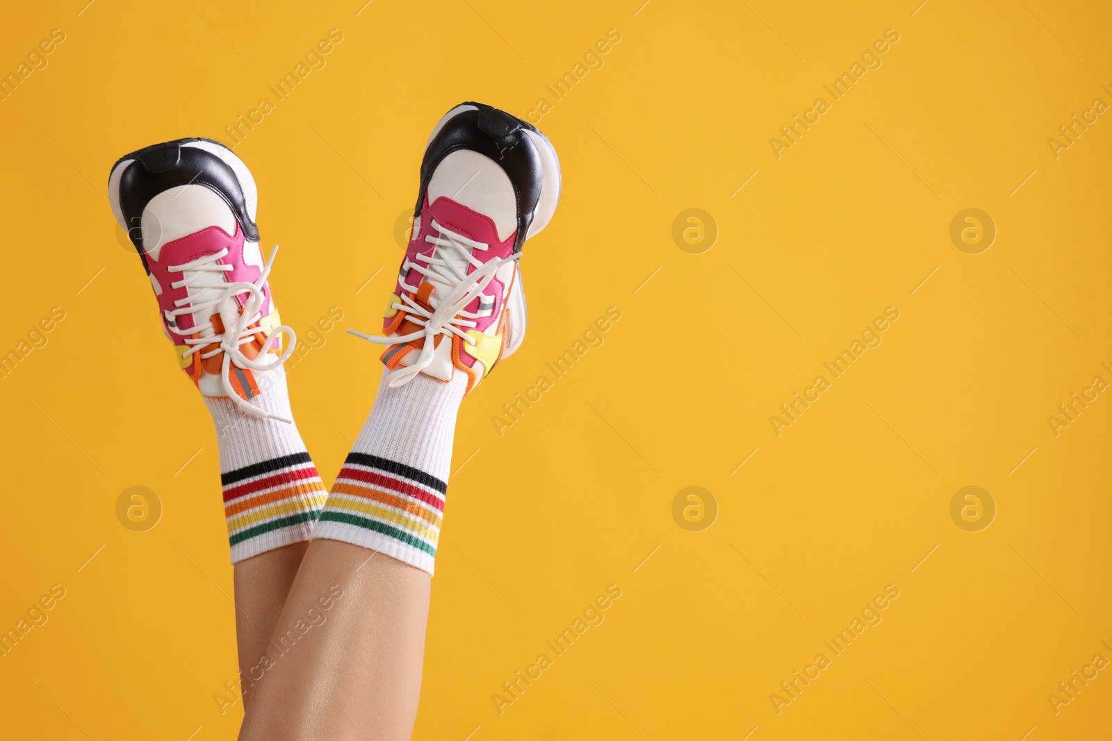 Photo of Woman wearing stylish sneakers on yellow background, closeup. Space for text