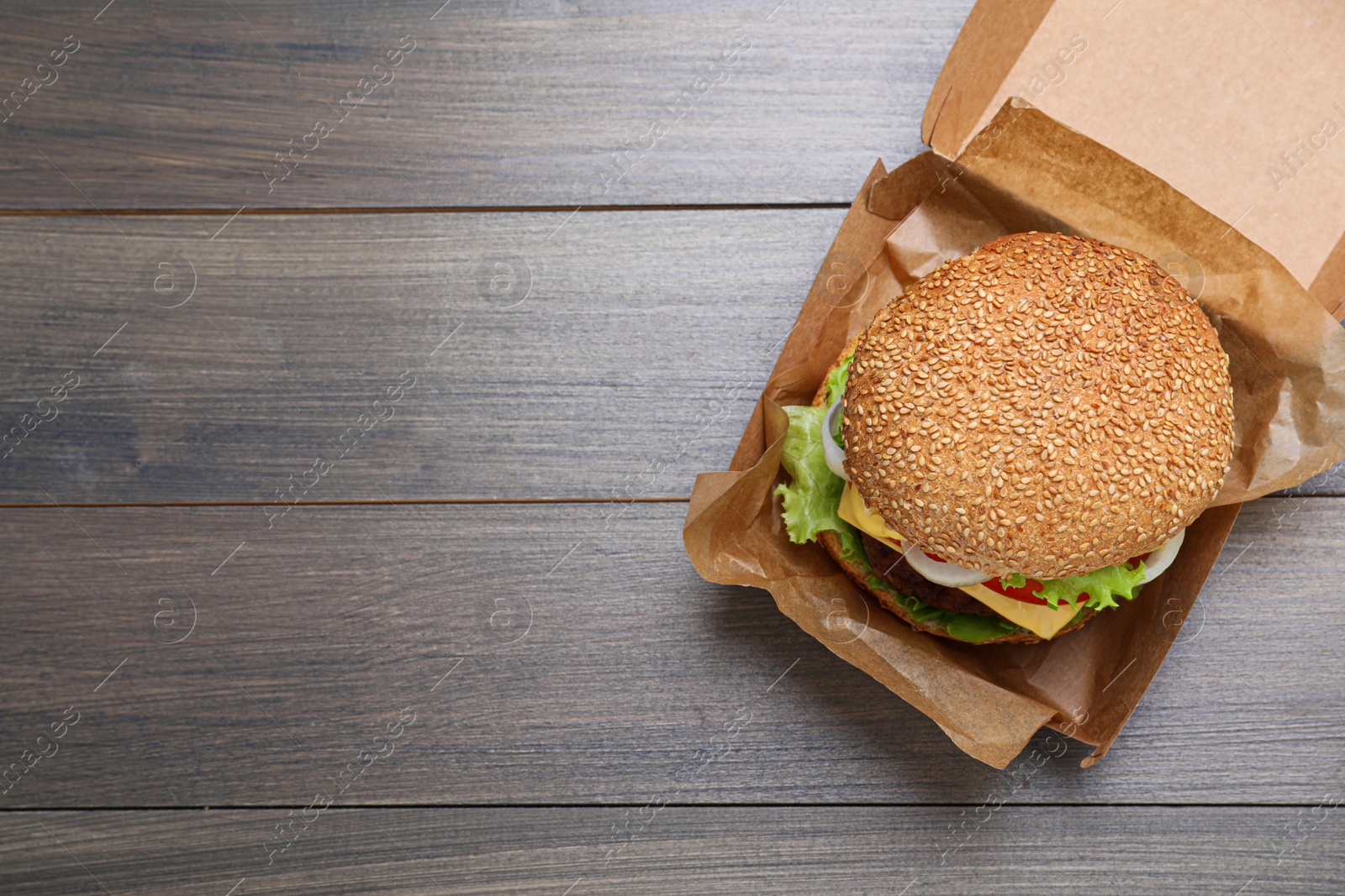 Photo of Delicious burger in cardboard box on wooden table, top view. Space for text