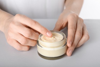 Photo of Woman with jar of body cream at grey table, closeup