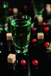 Photo of Absinthe in shot glass, cranberries and brown sugar on mirror table, closeup. Alcoholic drink