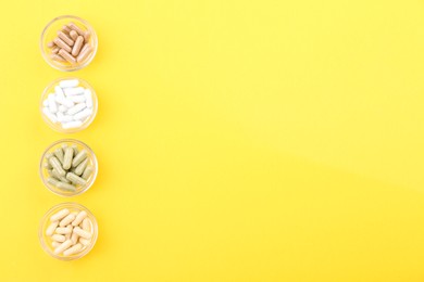 Photo of Different vitamin capsules in glass bowls on yellow background, flat lay. Space for text