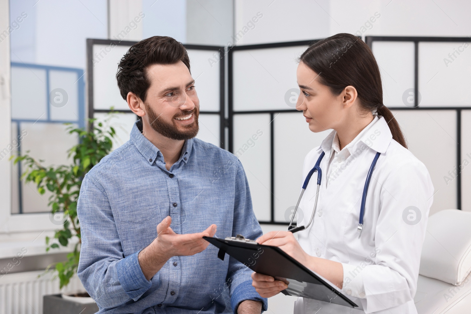 Photo of Doctor with clipboard consulting patient during appointment in clinic