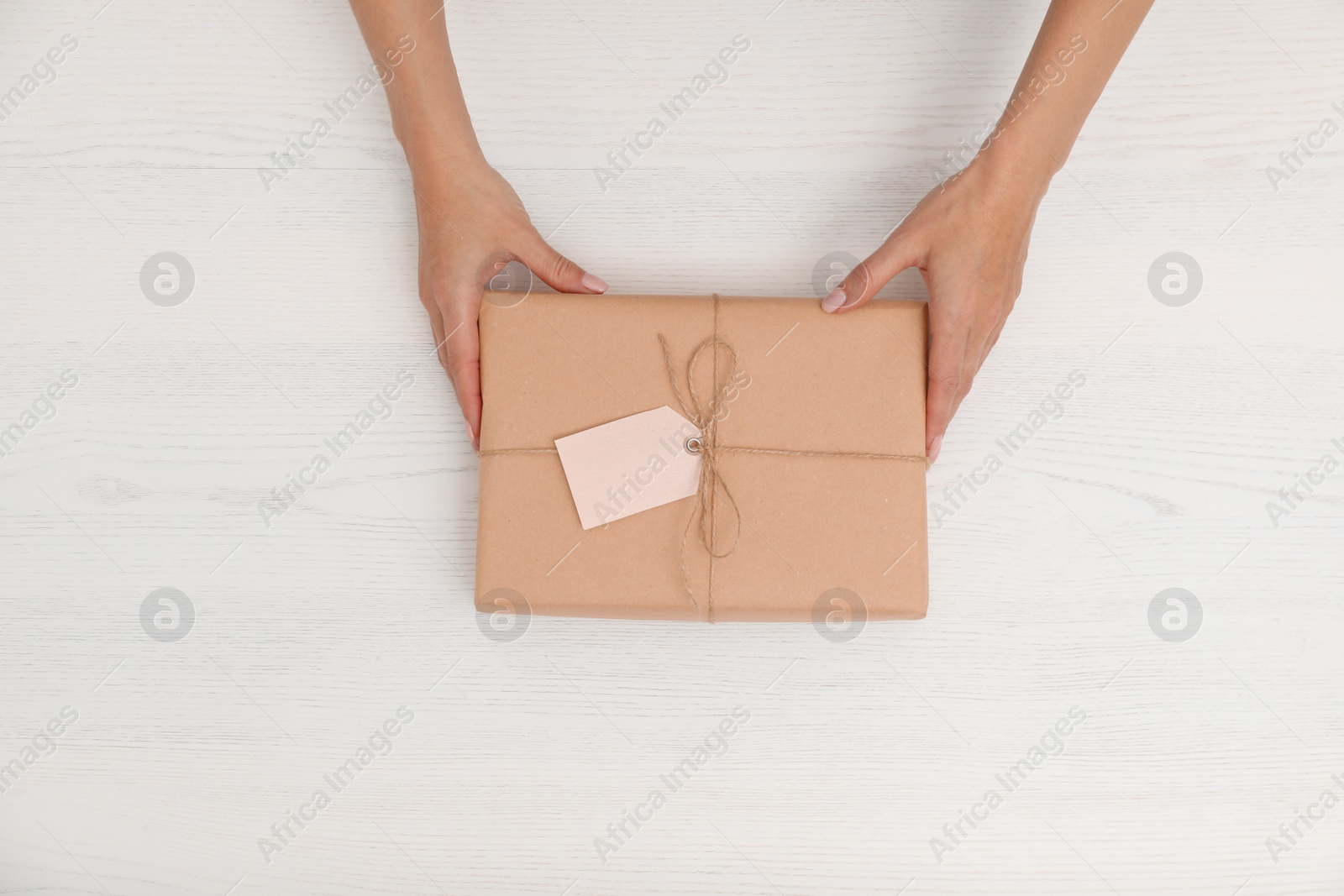 Photo of Woman holding parcel with tag on wooden background, top view