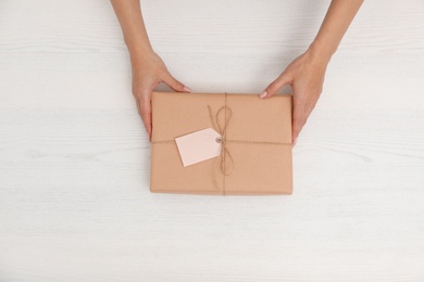 Woman holding parcel with tag on wooden background, top view