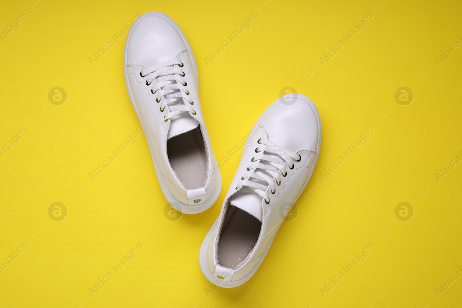 Photo of Pair of stylish white sneakers on yellow background, top view