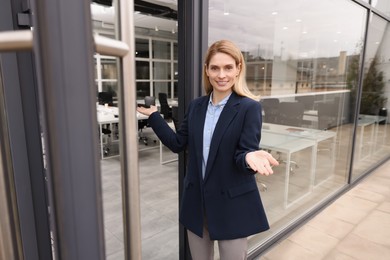 Happy real estate agent in suit inviting inside