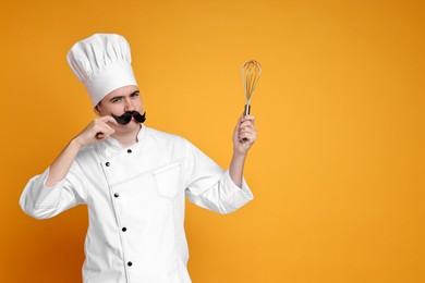 Photo of Portrait of happy confectioner with funny artificial moustache holding whisk on orange background, space for text