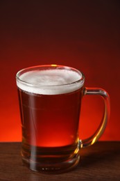 Mug with fresh beer on wooden table against color background