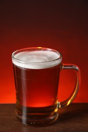 Photo of Mug with fresh beer on wooden table against color background