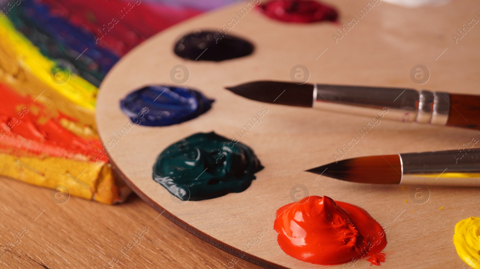 Photo of Artist's palette with samples of colorful paints and brushes on wooden table, closeup