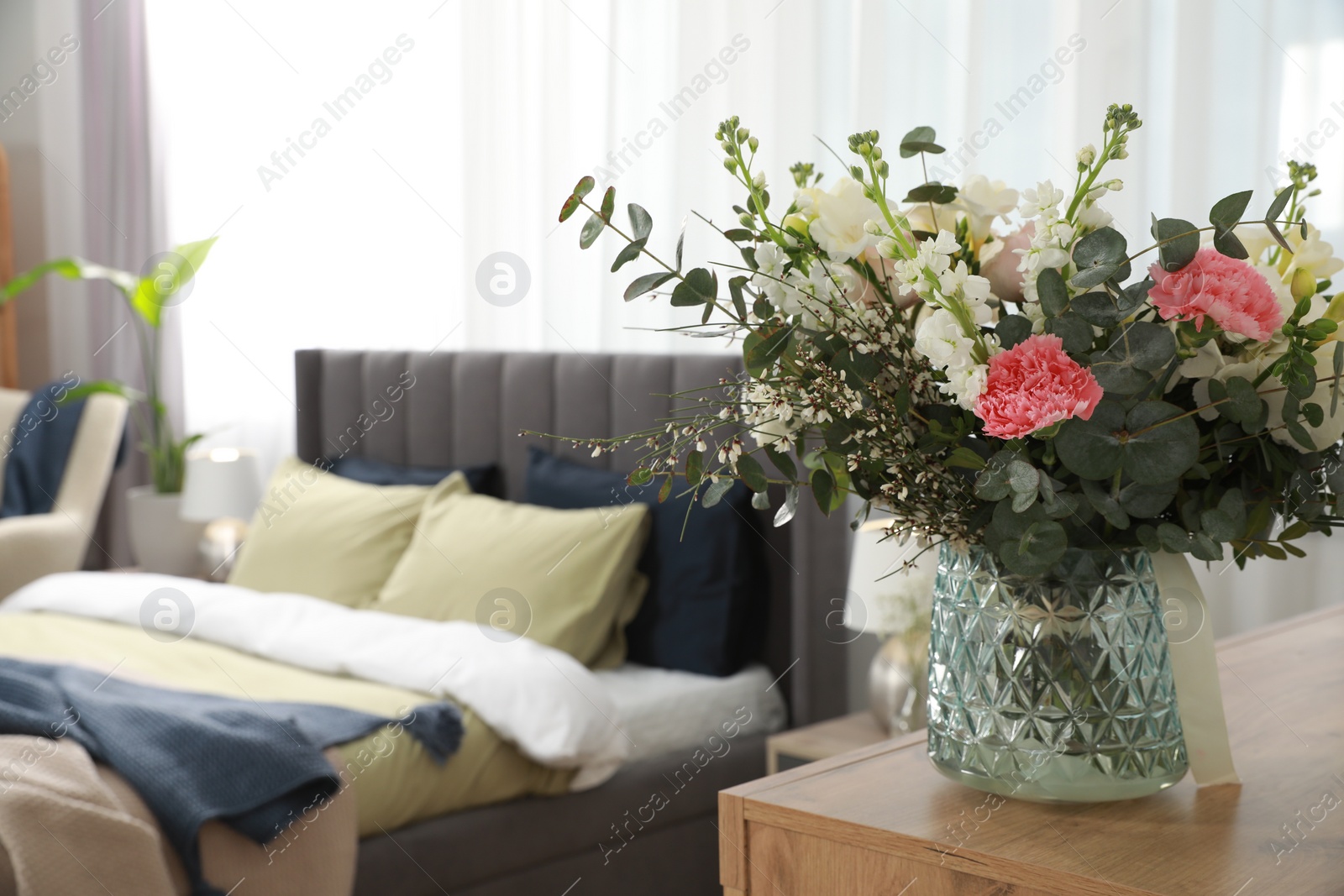 Photo of Large comfortable bed in room, focus on beautiful bouquet, space for text. Stylish interior