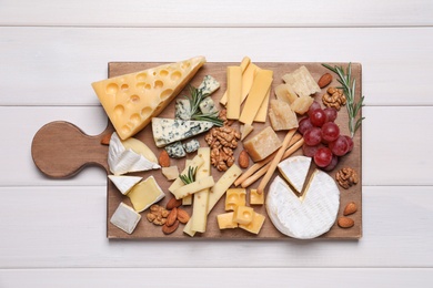 Cheese plate with grapes and nuts on white wooden table, top view