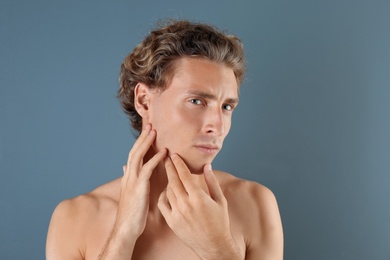 Young man touching his soft skin after shaving on gray background