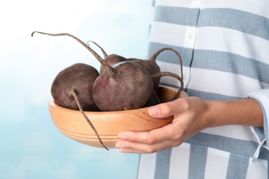 Woman holding bowl with beets on light background