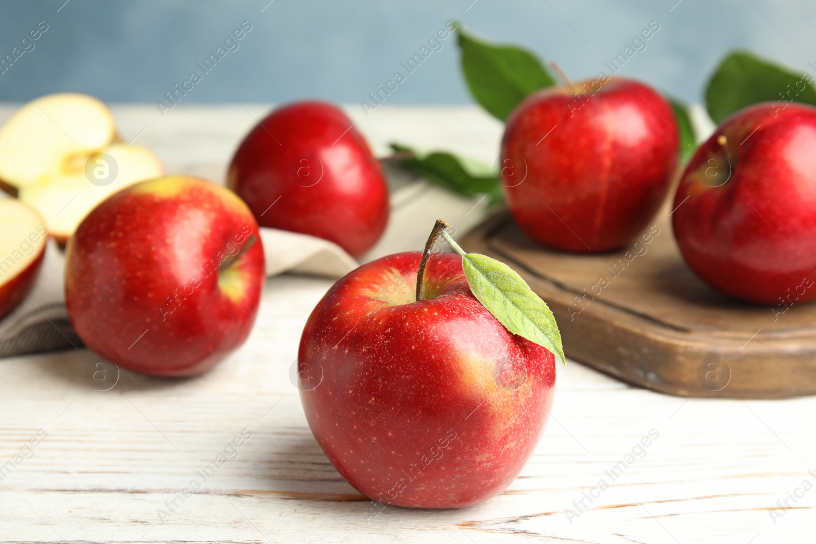 Photo of Ripe juicy red apples on white wooden table against blue background