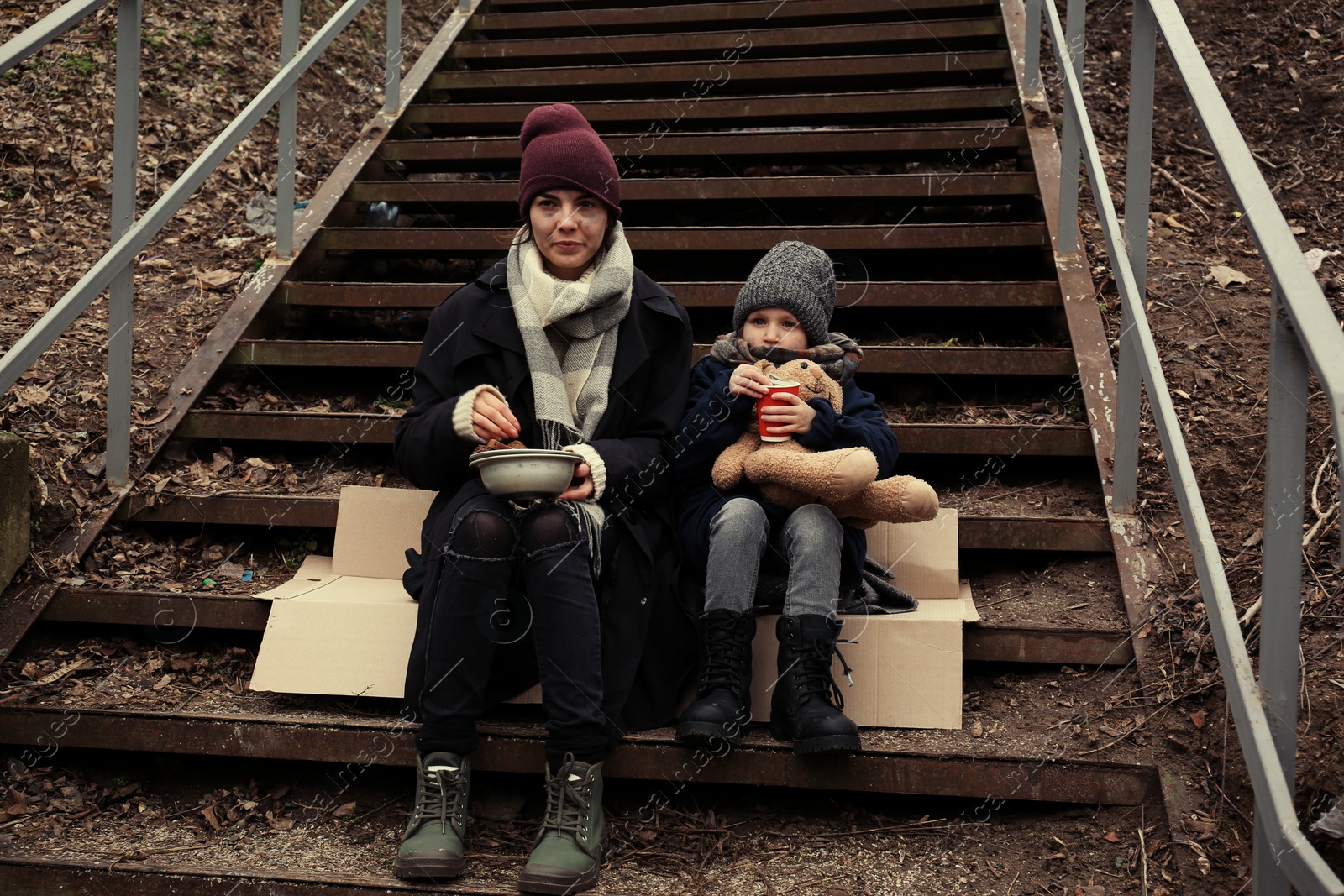 Photo of Poor mother and daughter with bread sitting on stairs outdoors