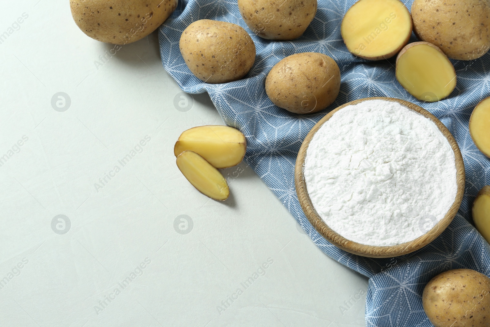 Photo of Bowl with starch and fresh potatoes on white table, flat lay. Space for text