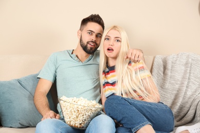 Photo of Young couple with bowl of popcorn watching TV on sofa at home
