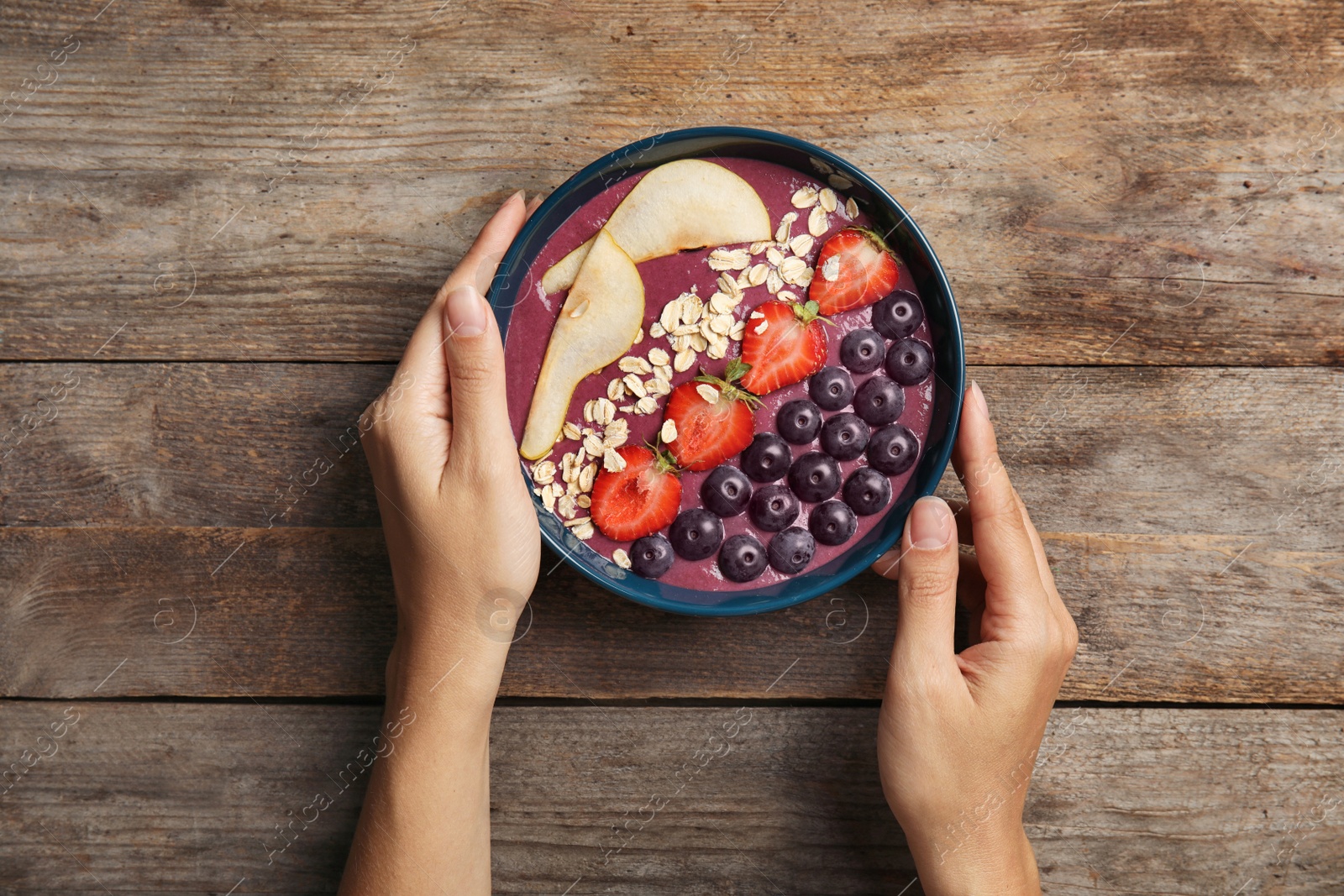 Photo of Woman holding bowl of tasty acai smoothie on wooden table