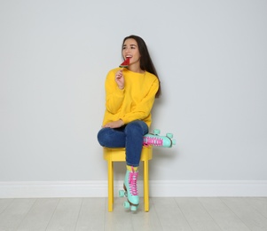 Young woman with roller skates and lollipop sitting on chair near color wall